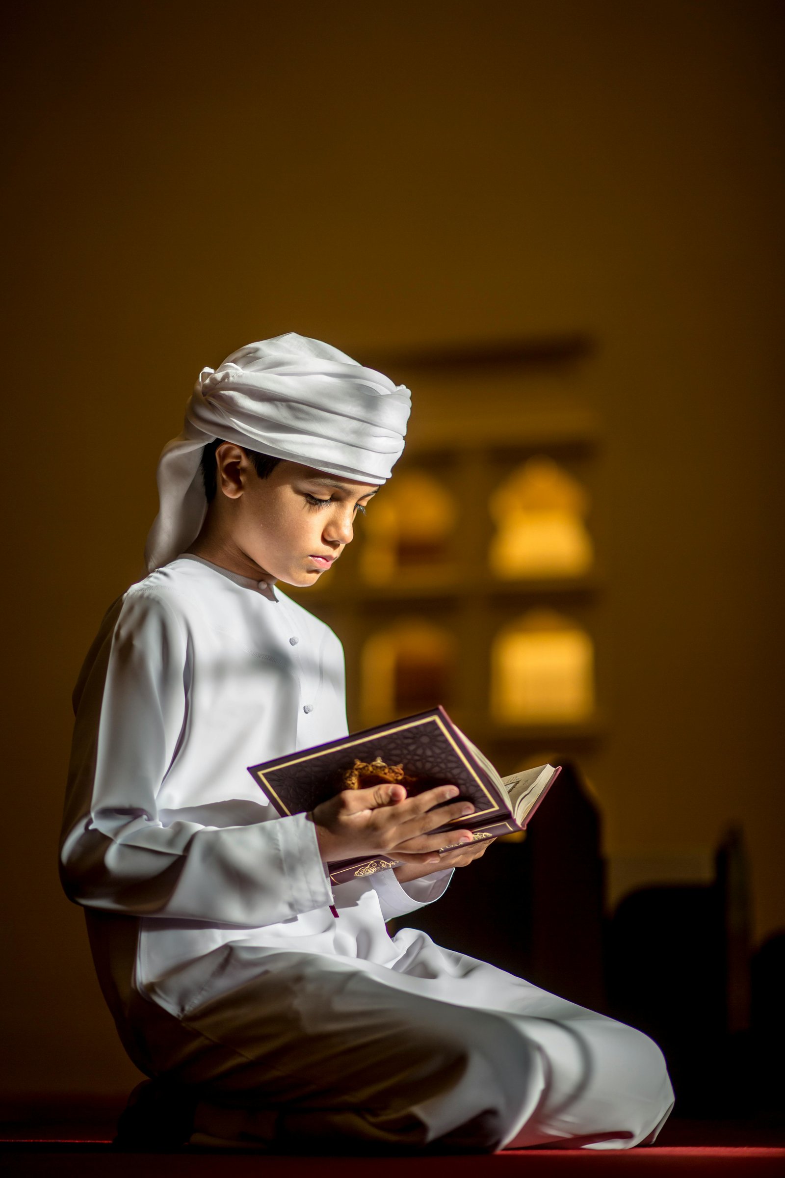 Young boy in traditional attire reading Quran in a peaceful Islamic classroom setting