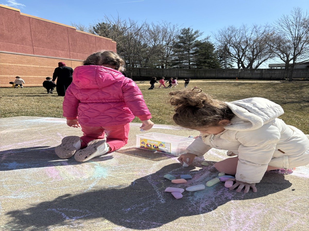 Children creating chalk drawings outdoors during a sunny day activity at Iqra Learning
